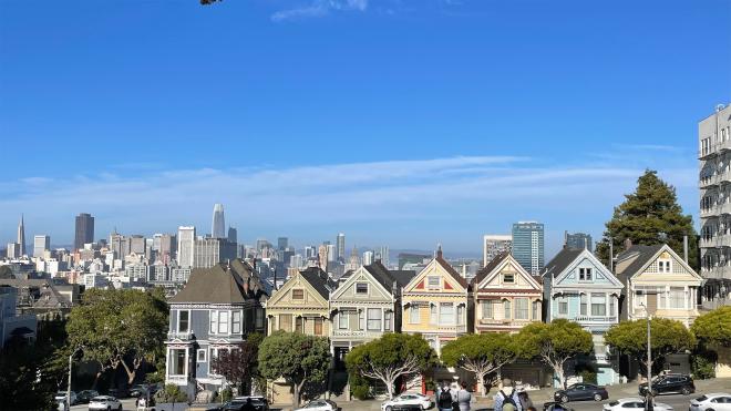 一排繽紛色彩的房屋排列在山坡上，背景是高樓大廈林立的舊金山市區