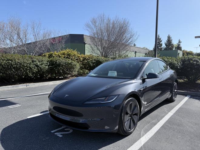 停在戶外停車格中的特斯拉 Model 3 電動車,車身為深灰色