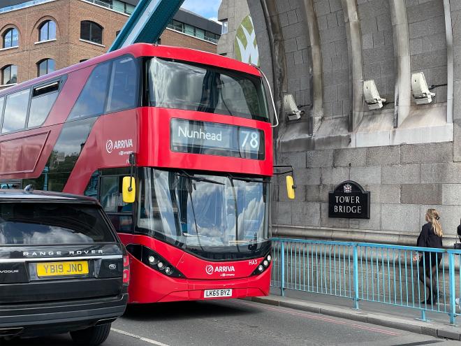 紅色的倫敦公車在倫敦塔橋的名牌旁